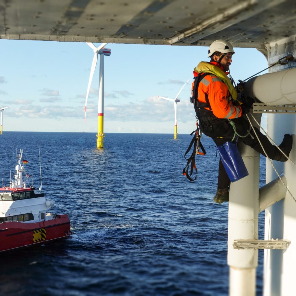Man werkt aan platform op zee met uitzicht op boot en windmolen