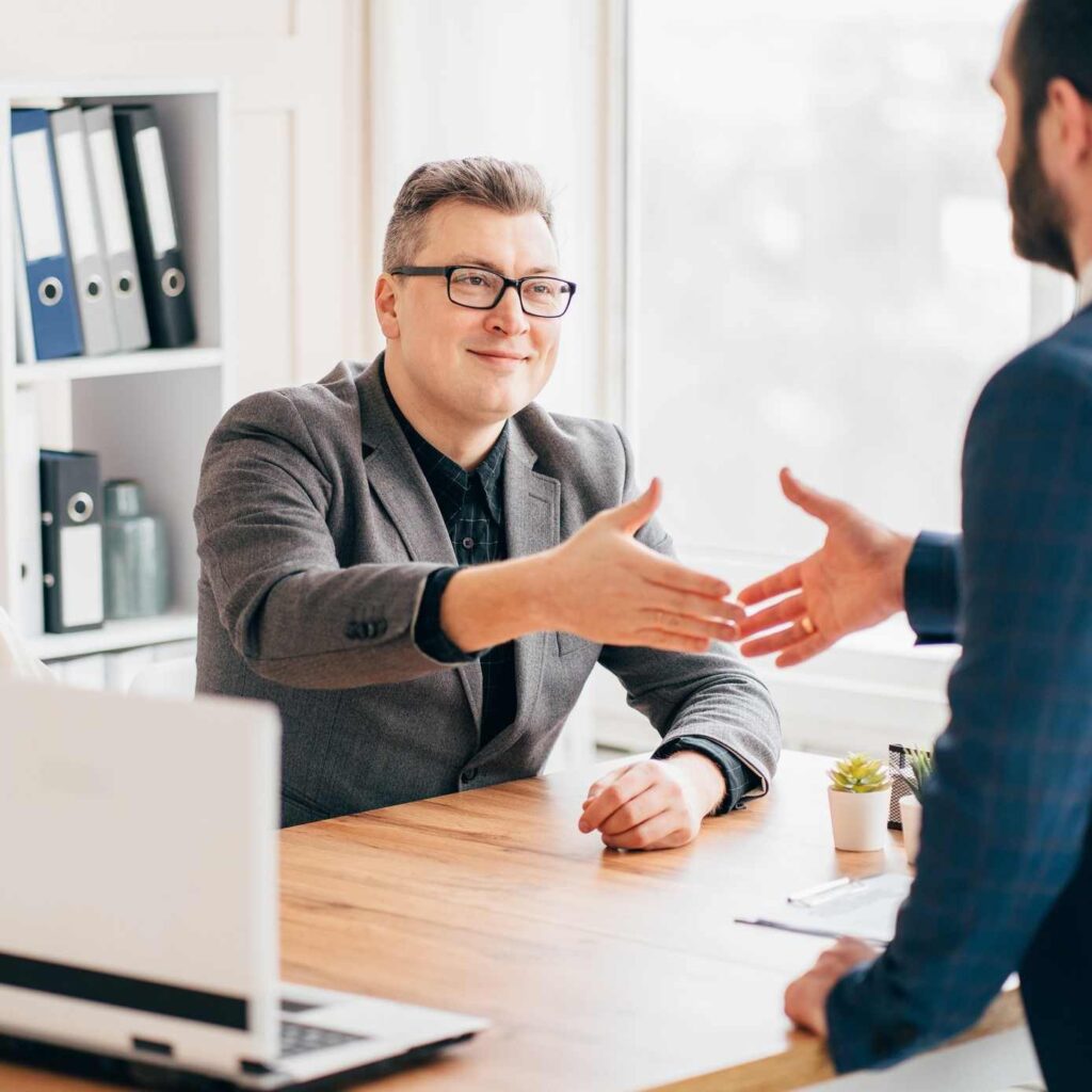 Man met bril geeft andere man over tafel een hand