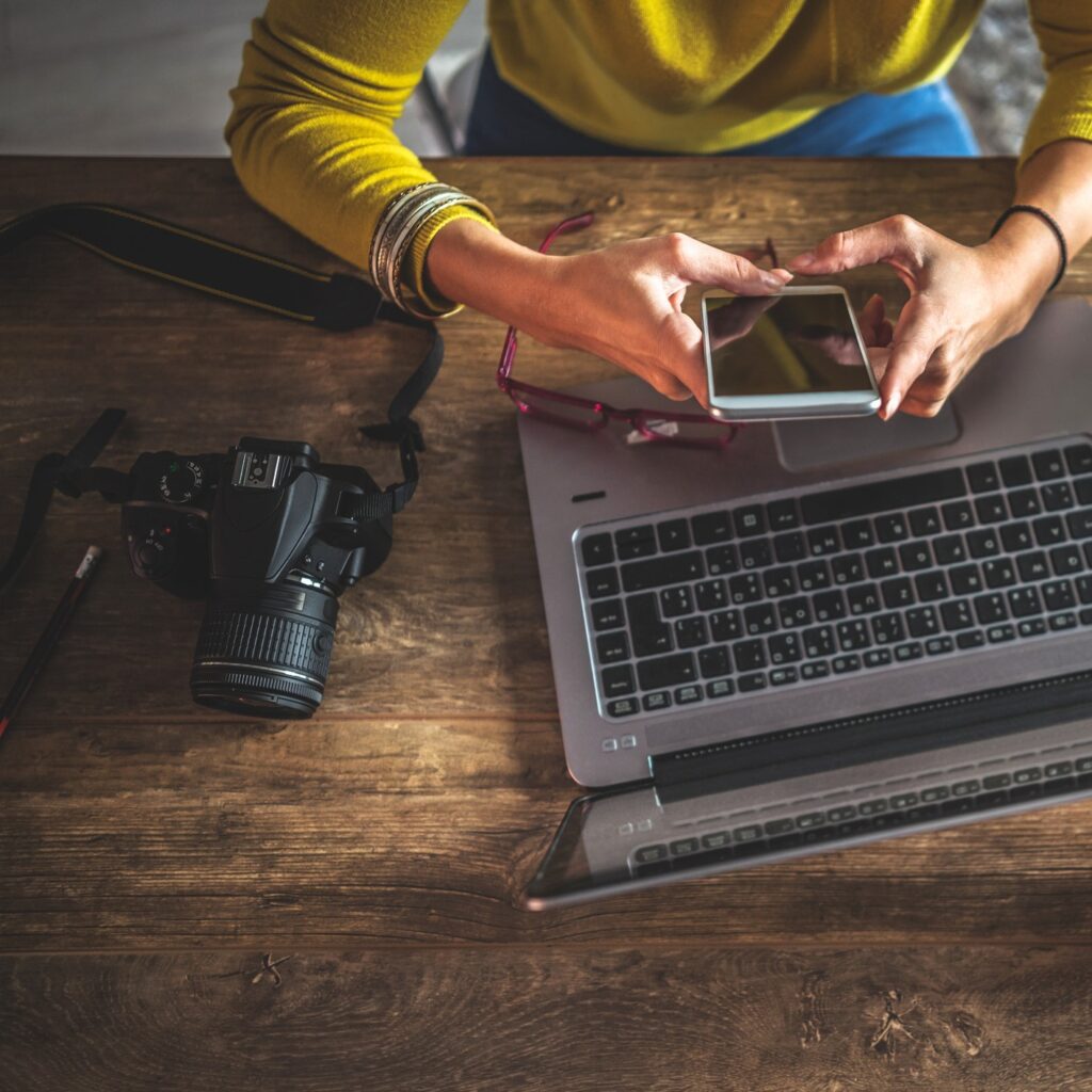 Vrouw kijk op telefoon terwijl ze achter laptop zit