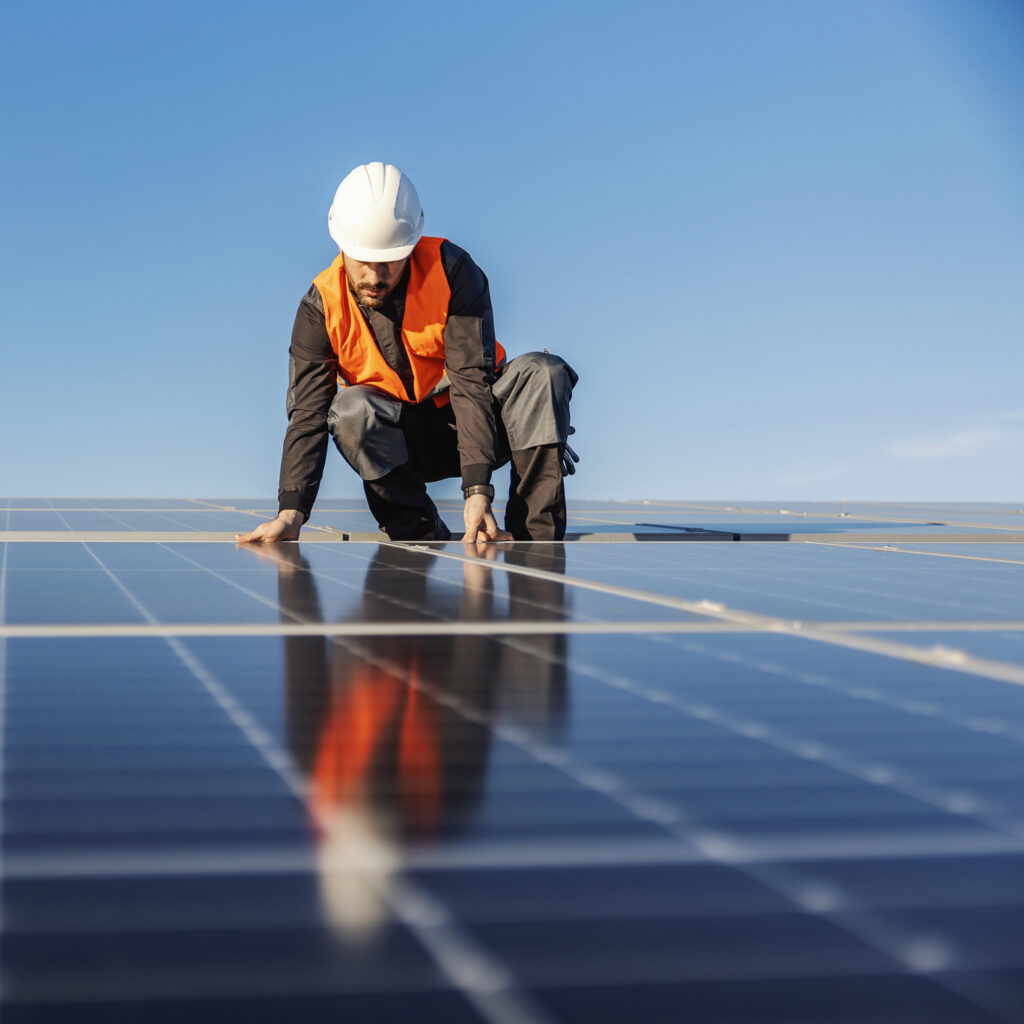 Man met helm installeert zonnepanelen op dak