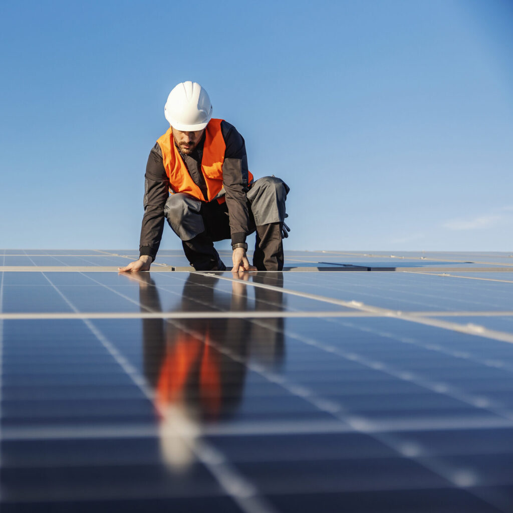 Man met helm installeert zonnepanelen op dak