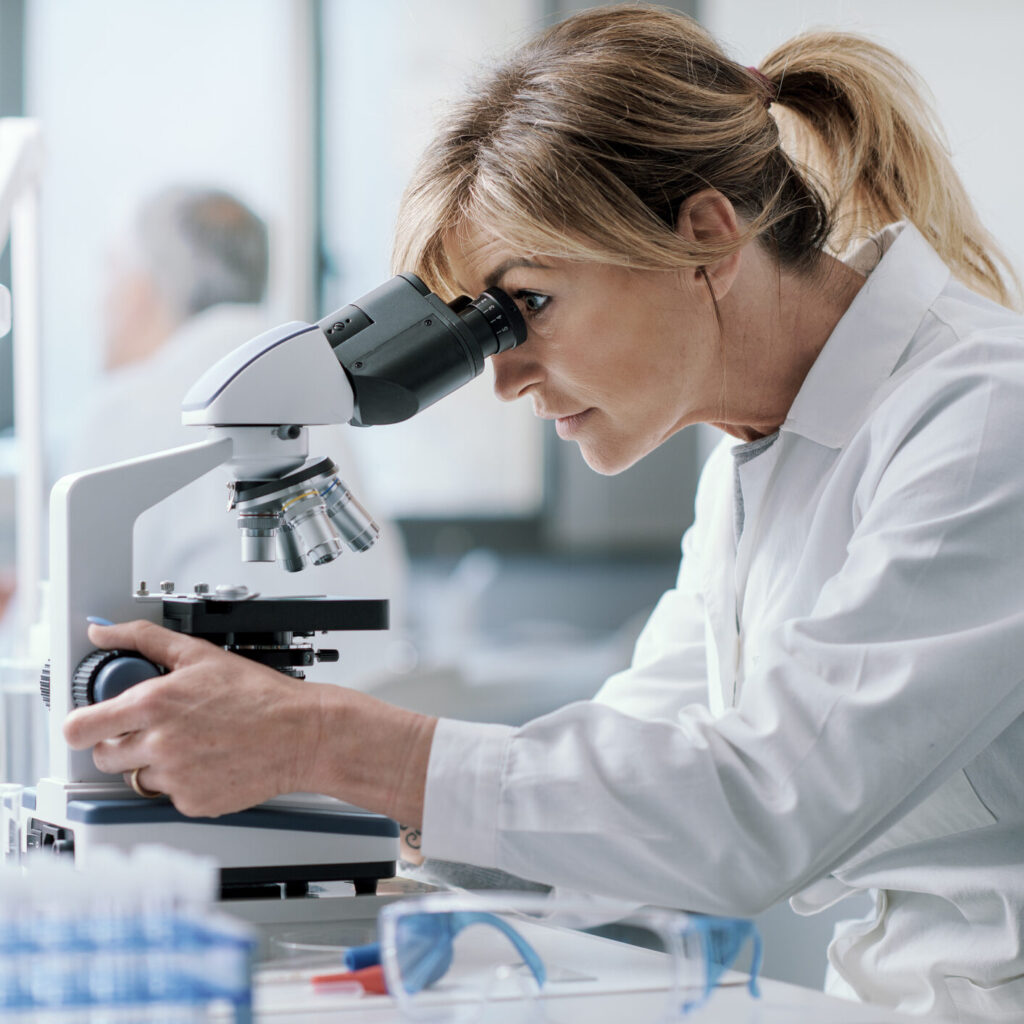 Professional female scientist working in the laboratory, she is looking through a microscope, medical research concept